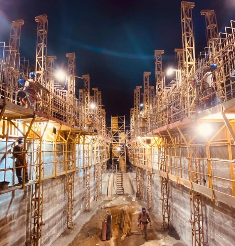 Obra industrial noturna com andaimes e equipe em campo